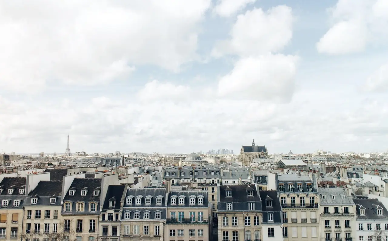 Façades en pierre et toits mansardés d'immeubles parisiens avec balcons sous un ciel nuageux, la tour Eiffel au loin
